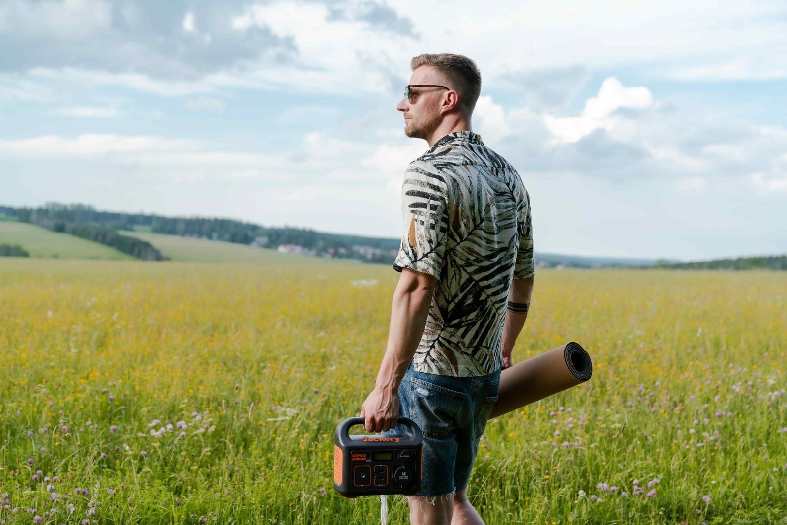 A Jackery Explorer portable power station carried by hand across open ground at golden hour.
